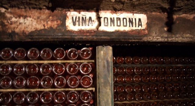 Botellas de vino blanco dispuestas horizontalmente en el calado de la bodega. Sobre los estantes, un cartel antiguo con el nombre de la marca: Viña Tondonia.