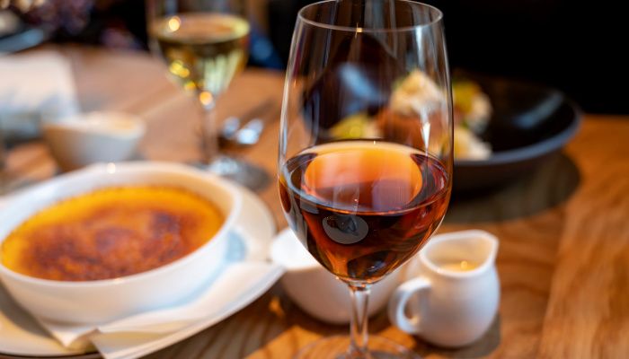 Copa de postre con vino dulce en un tercio de su capacidad, en una mesa con un plato de crema catalana caramelizada.