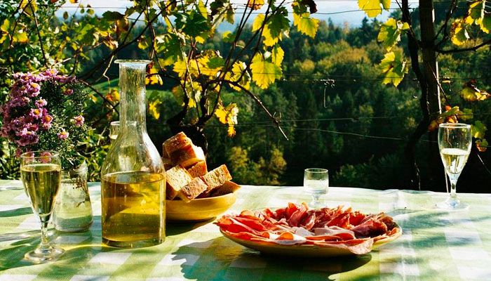 A table in a garden servei with a bottle of yellow-coloured wine and slived ham and bread.