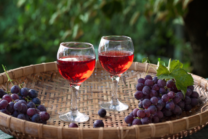 Wicker tray with two glasses full of rosé wine, bunches of small-grain black grapes, ripe. Photo by Nadine from Pixabay.