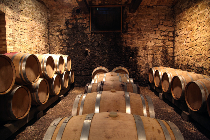 Rows of barrels filled with wine, in a stone-walled cellar. Photo by Tamara Malaniy from Unsplash.