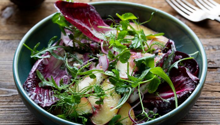 Bol de ensalada de hojas verdes y moradas y melocotón blanco.