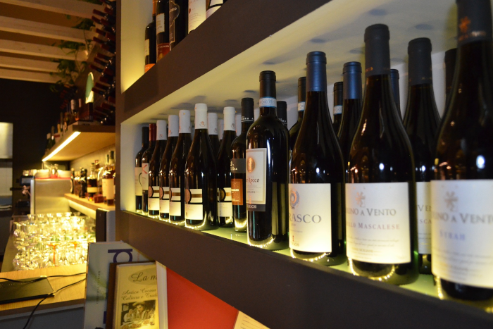 Shelves illuminated with dim led light, from a bar shop, filled with bottles of wine. Table full of empty glasses, ready to use. Photo by Orazio Foti from Pixabay.