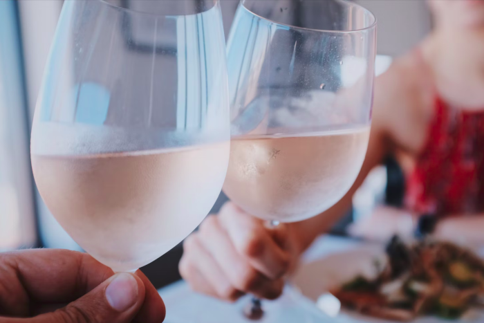 Two hands toasting with a light rosé wine. Foto by Vincenzo Landino from Unsplash.