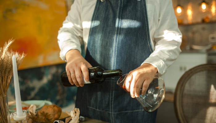 A person wearing an apron pouring wine into a decanter.