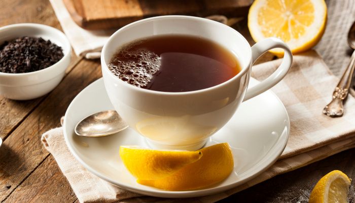 A cup of tea with a slice of lemon and some tea leaves on the side.