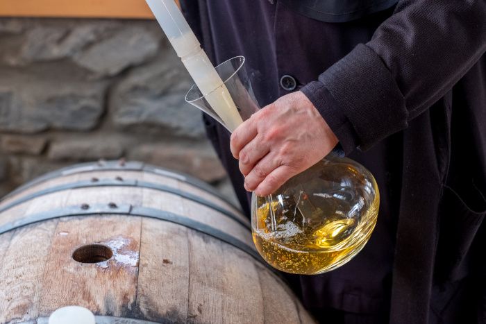 Bodeguero vertiendo un poco de vino de color amarillo muy intenso en un decantador tras sacarlo de una barrica de roble.