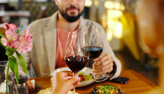 Two people at a restaurant toasting their wine glasses one-third full.