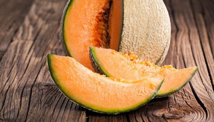 A Galia melon open with two slices in front showing its orange flesh.